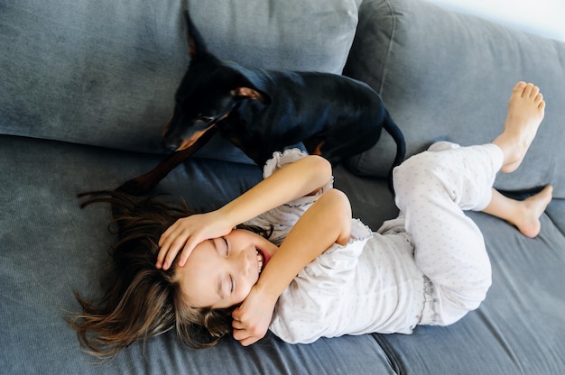 Das Mädchen mit dem Hund spielt auf dem Sofa