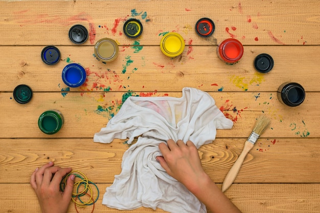 Das Mädchen rollt ein weißes T-Shirt zum Malen im Stil von Tie Dye auf