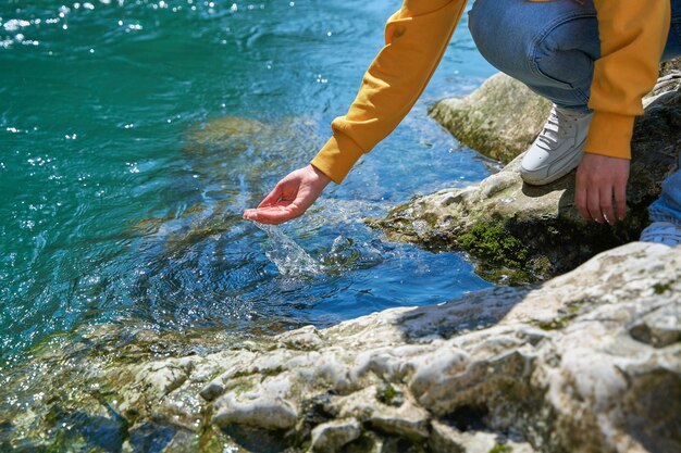 Das Mädchen sammelt kristallklares Wasser aus einem Bergfluss in ihrer Handfläche