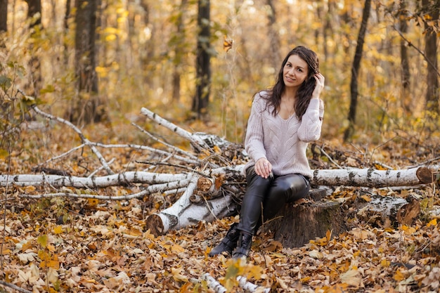 Das Mädchen setzte sich auf einen Baumstumpf im gelben Herbstwald mit Blättern