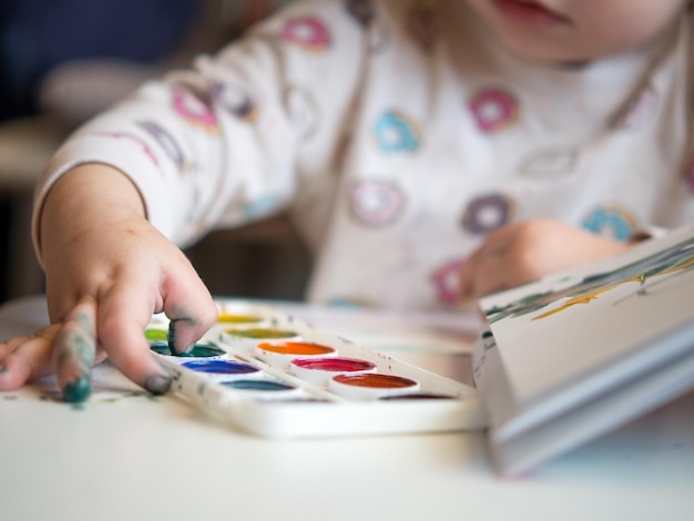 Das Mädchen sitzt am Tisch und zeichnet mit den Fingern in das Skizzenbuch Kreativität der Kinder Hobbys der Kinder
