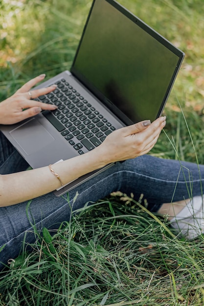 Das Mädchen sitzt auf dem Rasen und verwendet einen Laptop. Bildungs-Lifestyle-Technologie-Konzept Outdoor-Lernkonzept