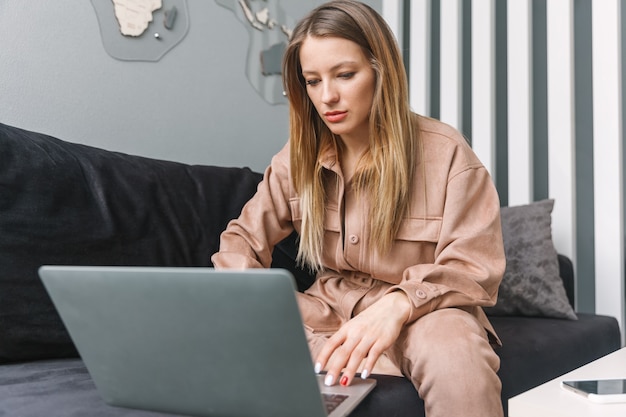 Das Mädchen sitzt auf der Couch und arbeitet am Laptop