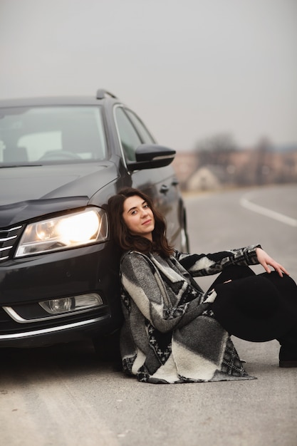 Das Mädchen sitzt auf der Straße in der Nähe eines schwarzen Autos