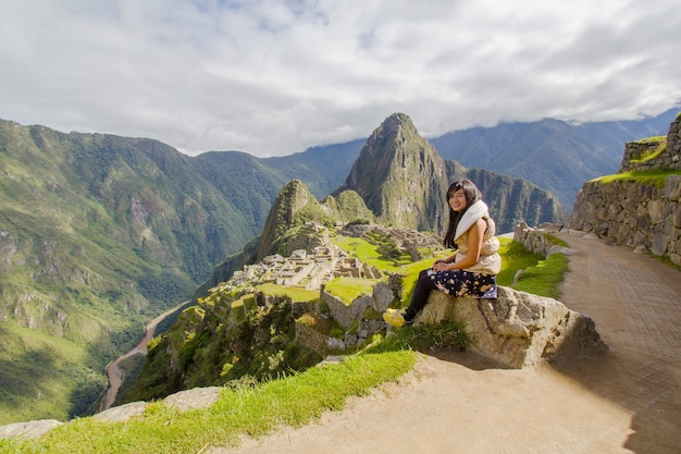 Das Mädchen sitzt auf Stein mit einer Landschaftsansicht von Machupicchu sieben Wunder dieser Welt in Peru.
