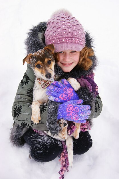 Das mädchen sitzt im schnee und hält in den händen ihres geliebten hundes. glückliche kindheit. liebe zu tieren