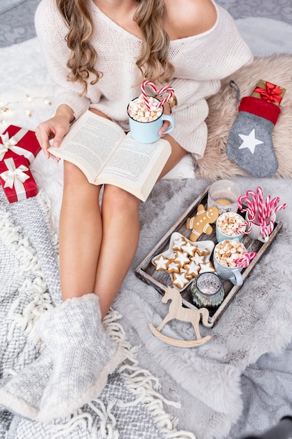 Das Mädchen sitzt in weihnachtlicher Atmosphäre, trinkt ein heißes Getränk und liest ein Buch.
