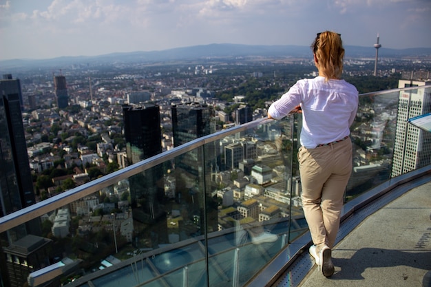 Das Mädchen steht auf einem hohen Turm in der Stadt Frankfurn am Main und schaut sich die Stadt an