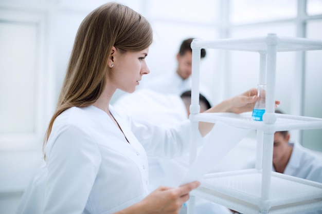 Das Mädchen steht im wissenschaftlichen Labor und betrachtet die Flasche mit einer chemischen Substanz
