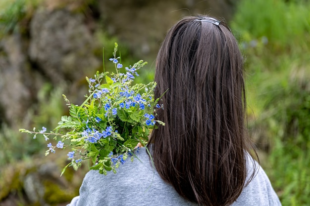 Das Mädchen trägt einen im Frühlingswald gesammelten Blumenstrauß, Ansicht von hinten.