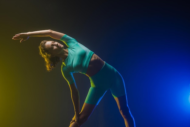 Das Mädchen trainiert auf dunklem Hintergrund moderne Fitness auf gelbblauem Hintergrund mit Platz für Text