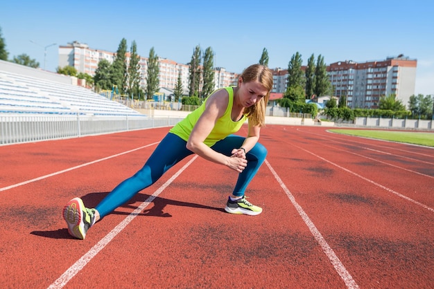 Das Mädchen wärmt sich im Stadion auf Sportlerin dehnt die Beinmuskulatur vor dem Joggen Training im Sportstadion der Stadt