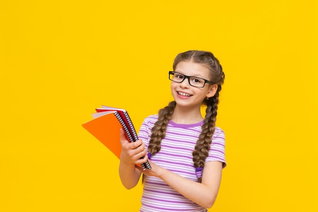 Das Mädchen zeigt ihre Notebooks und freut sich ein Kind auf gelbem Hintergrund Ein kleines Mädchen mit Brille