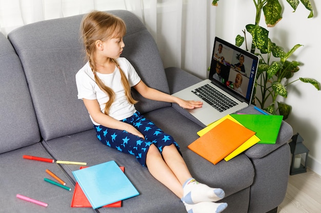 Das Mädchen zu Hause kommuniziert mit Freunden im Internet. Fernunterricht für Kinder. Nettes kleines Mädchen, das zu Hause Laptop verwendet. Bildung, Online-Studium, Heimstudium, Schulmädchen-Kinder-Lifestyle-Konzept