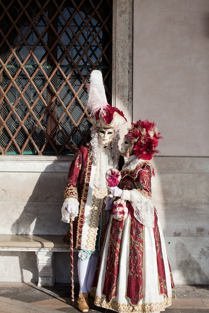 Das maskierte Paar in kunstvollem Kostüm an der venezianischen Maskerade steht an einer Steinmauer in der Nähe des Markusplatzes in Venedig