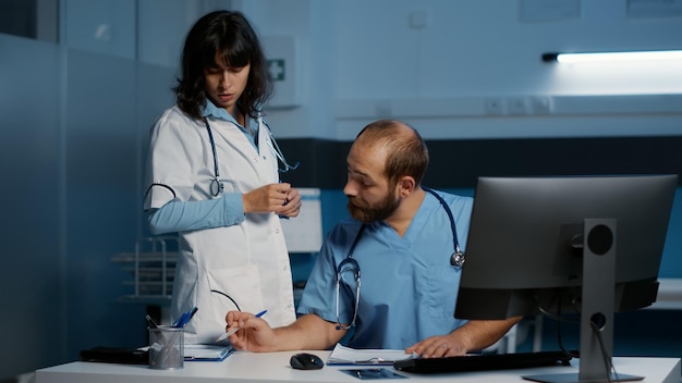 Das medizinische Team analysiert den Krankheitsbericht des Patienten am Computer, während es über Stunden im Krankenhausbüro arbeitet. Arzt und Assistent planen Gesundheitsbehandlungen zur Heilung von Krankheiten. Medizinischer Dienst