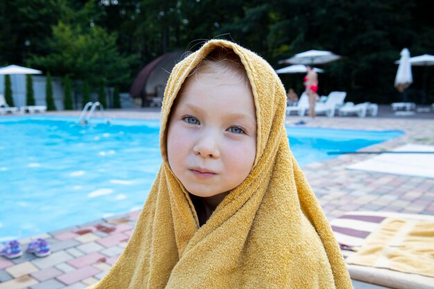 Das mit einem Handtuch bedeckte Mädchen sitzt in der Nähe des Pools