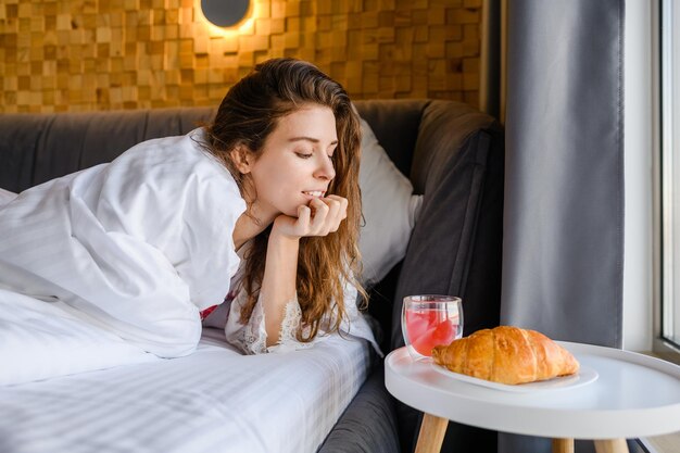 Das mit einer Decke bedeckte Mädchen wird im Bett frühstücken