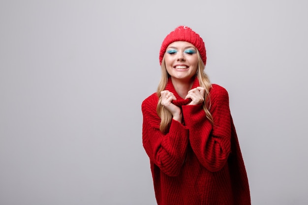 Das Model lächelt in einem Winterpullover und Make-up auf grauem Hintergrund, freier Platz für Text