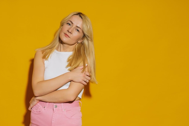 Das Model posiert im Studio auf gelbem Hintergrund Eine junge Frau in einem weißen Top und rosa Jeans Trendiges Hipster-Outfit