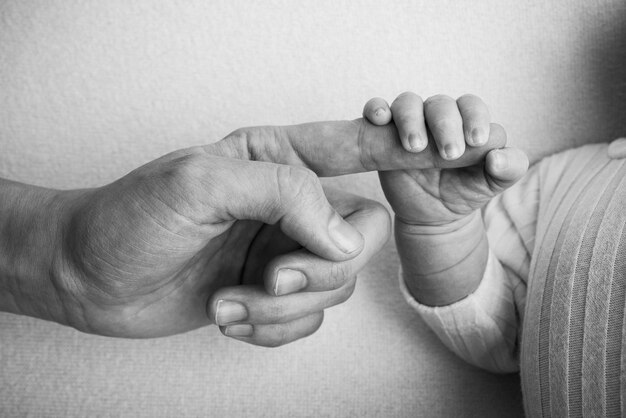 Das Neugeborene hat nach der Geburt den Finger der Eltern fest im Griff. Close-up kleine Hand des Kindes und Palme von Mutter und Vater. Elternschaft, Kinderbetreuung und Gesundheitskonzept. Schwarzweißfoto.