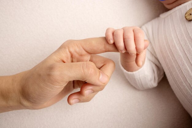 Das Neugeborene in einer weißen Hose hat nach der Geburt den Finger der Eltern fest im Griff. Close-up kleine Hand des Kindes und Palme von Mutter und Vater. Elternschaft, Kinderbetreuung und Gesundheitskonzept.