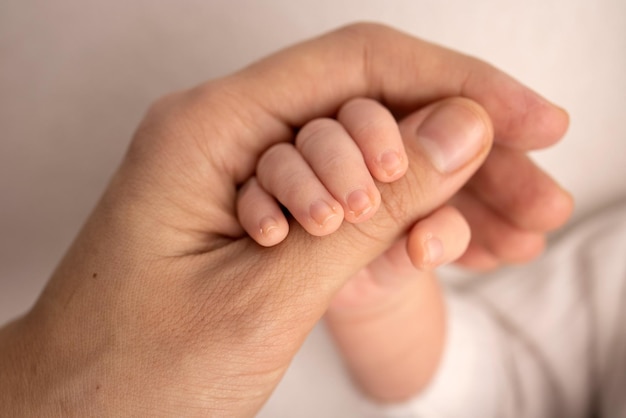 Das Neugeborene in einer weißen Hose hat nach der Geburt den Finger der Eltern fest im Griff. Close-up kleine Hand des Kindes und Palme von Mutter und Vater. Elternschaft, Kinderbetreuung und Gesundheitskonzept.