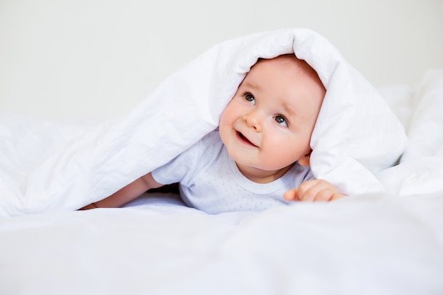 Das niedliche lächelnde Baby liegt im Bett des Hauses. Bettwäsche für Kinder