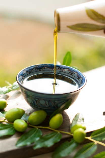 Das Olivenöl in der Tasse. Zweig eines Olivenbaums mit frischen Oliven. Grüne Oliven. Im Garten. Auf einem Holzbrett. ein Krug für Öl. Italienische Klassiker. Oliven aus Italien. Essen aus Italien