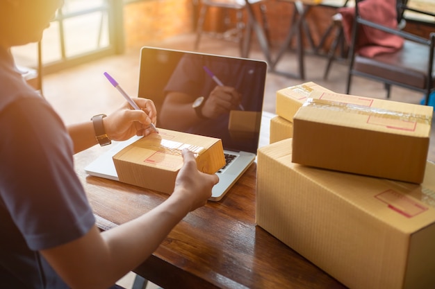 Das on-line-kaufende Junge beginnen Kleinunternehmen in einer Pappschachtel bei der Arbeit.