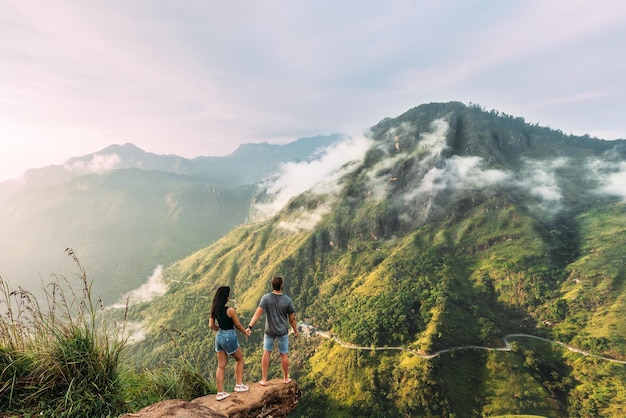 Foto das paar begrüßt den sonnenaufgang in den bergen. junge und mädchen in den bergen. mann und frau, die händchen halten. das paar reist durch asien. reise nach sri lanka. serpentinen in den bergen. flitterwochen