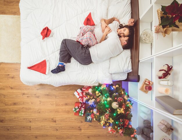 Das Paar lag auf dem Bett neben dem Weihnachtsbaum. von oben betrachten