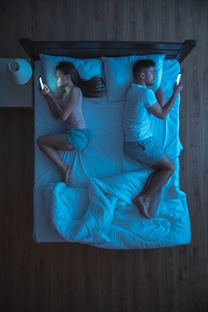 Das Paar mit Smartphone lag auf dem Bett. Nachtansicht. von oben