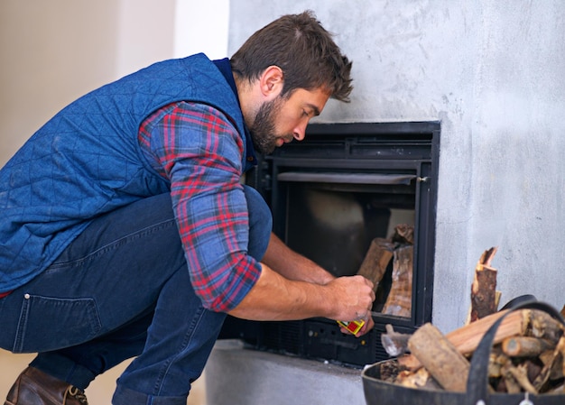 Das perfekte Feuer machen Aufnahme eines jungen Mannes, der zu Hause in seinem Kamin ein Feuer macht