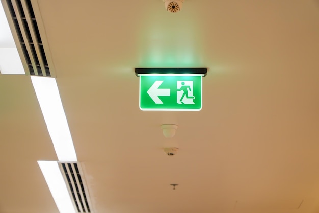 Das Pfeil-Leuchtkasten-Schild des NOTFEUERAUSGANGS ist an der Decke in Krankenhausideen für Brandfälle aufgehängt