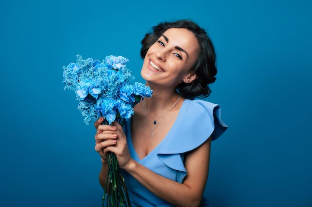 Das Porträt einer glücklichen, aufgeregten, wunderschönen jungen Frau in einem eleganten blauen Kleid posiert mit einem frischen Strauß blauer Blumen. Muttertag. Feiertage für Frauen. Frühling. Frauenrechte