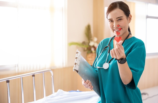 Das Porträt einer lächelnden Krankenschwester oder eines medizinischen Personals macht in einem Krankenhaus ein Mini-Herz-Handzeichen