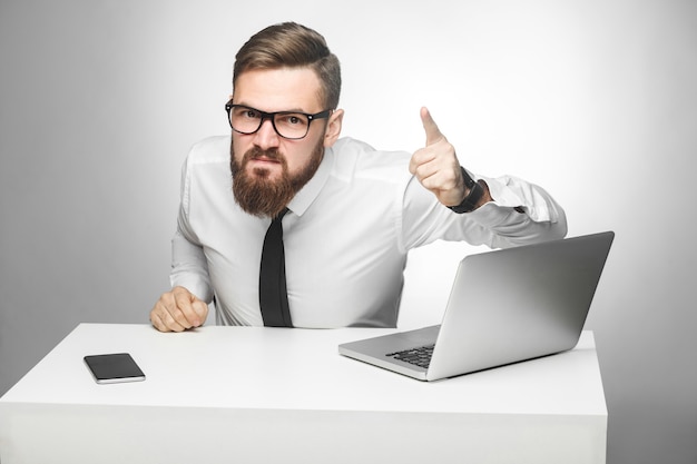 Das Porträt eines aggressiven, unglücklichen jungen Geschäftsmannes in weißem Hemd und schwarzer Krawatte beschuldigt Sie im Büro und hat schlechte Laune, schreit und zeigt mit geöffnetem Mund mit dem Finger auf Sie. Innenaufnahme, Studioaufnahme