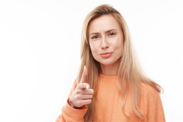 Das Porträt eines freundlichen blonden Mädchens wählt Sie aus und zeigt mit dem Finger auf die Kamera, die auf weißem Hintergrund isoliert ist