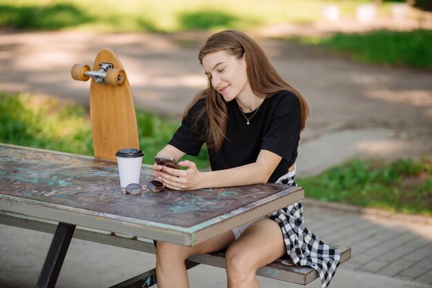 Das Porträt eines hübschen Teenager-Mädchens mit einem Skateboard sitzt und ruht sich auf der Bank im Freien im Skaterpark aus