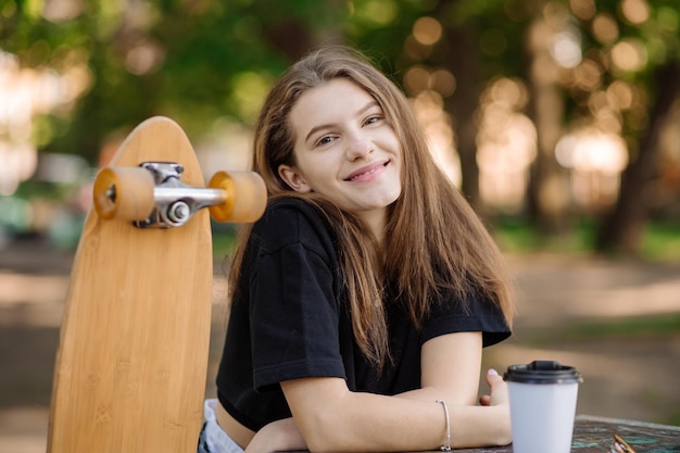 Das Porträt eines hübschen Teenager-Mädchens mit einem Skateboard sitzt und ruht sich auf der Bank im Freien im Skaterpark aus