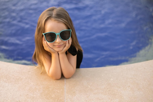 Das Porträt eines kaukasischen kleinen Mädchens legte ihre Hände auf den Rand des Pools und ihre Füße ins Wasser