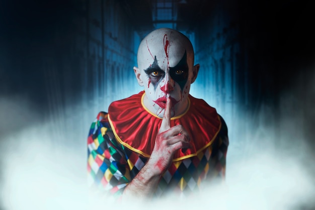 Das Porträt eines verrückten blutigen Clowns zeigt das ruhige Zeichen, Gesicht in Blut. Mann mit Make-up im Halloween-Kostüm, verrückter Verrückter