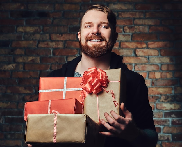Das positive Redbeard-Männchen hält Weihnachtsgeschenke über die Mauer eines Backsteins.