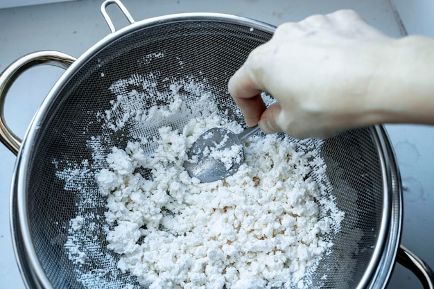 Das Reiben von Hüttenkäse durch ein Sieb, das köstlichen, krümeligen hausgemachten Hüttenkäse in einem Topf auf dem Tisch kocht, ist eine gesunde Draufsicht