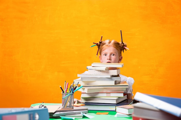 Das rothaarige Teenie-Mädchen mit vielen Büchern sitzt am Tisch im orangefarbenen Studio