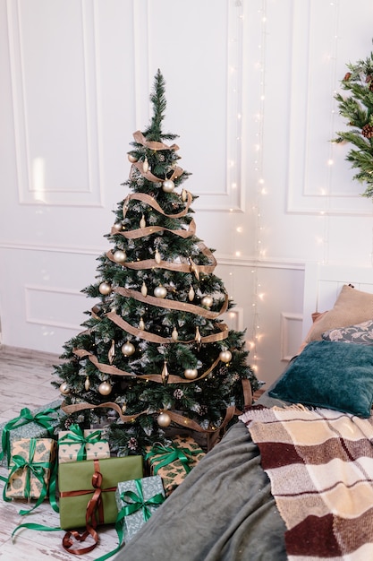 Das Schlafzimmer ist weihnachtlich dekoriert. Gemütliches helles Interieur: kariertes Holzbett. Im Zimmer steht ein mit Spielzeug und Girlanden geschmückter Weihnachtsbaum. Geschenke unter dem Baum