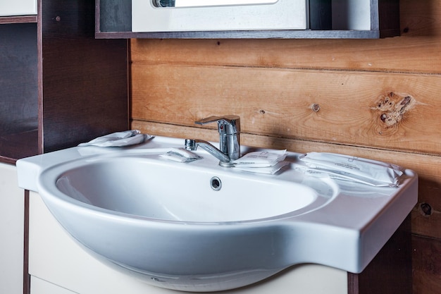 Das schneeweiße Keramikwaschbecken in der Nähe mit Hygieneprodukten im Badezimmer in einem Holzhaus