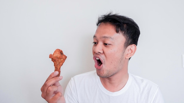 Das Schock- und Wow-Gesicht des jungen asiatischen Mannes isst gebratenes Huhn und trägt ein weißes Hemd
