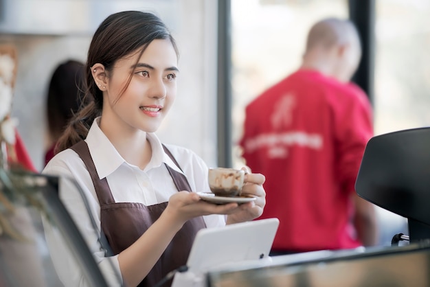 Das schöne barista, das heiße Kaffeetasse hält, diente dem Kunden mit lächelndem Gesicht am Bar coun